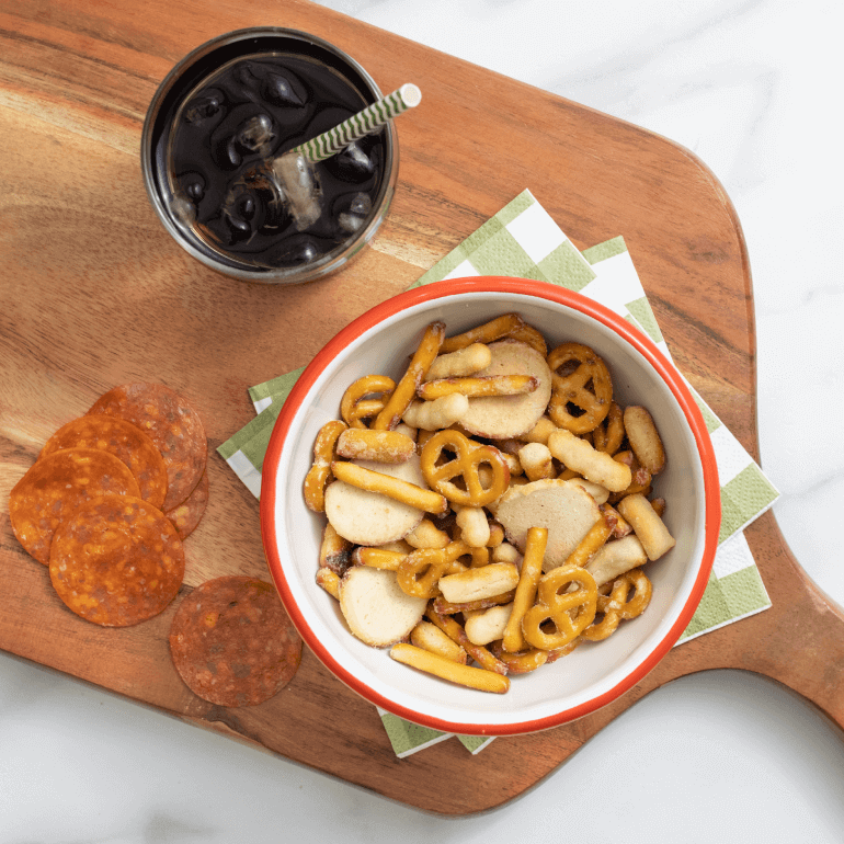 A bowl of Gardettos Italian Cheese blend on a cutting board with pepperoni and olives