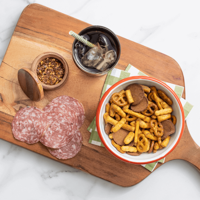 A bowl of Gardettos Spicy Italian blend on a cutting board with meat and crushed red peppers